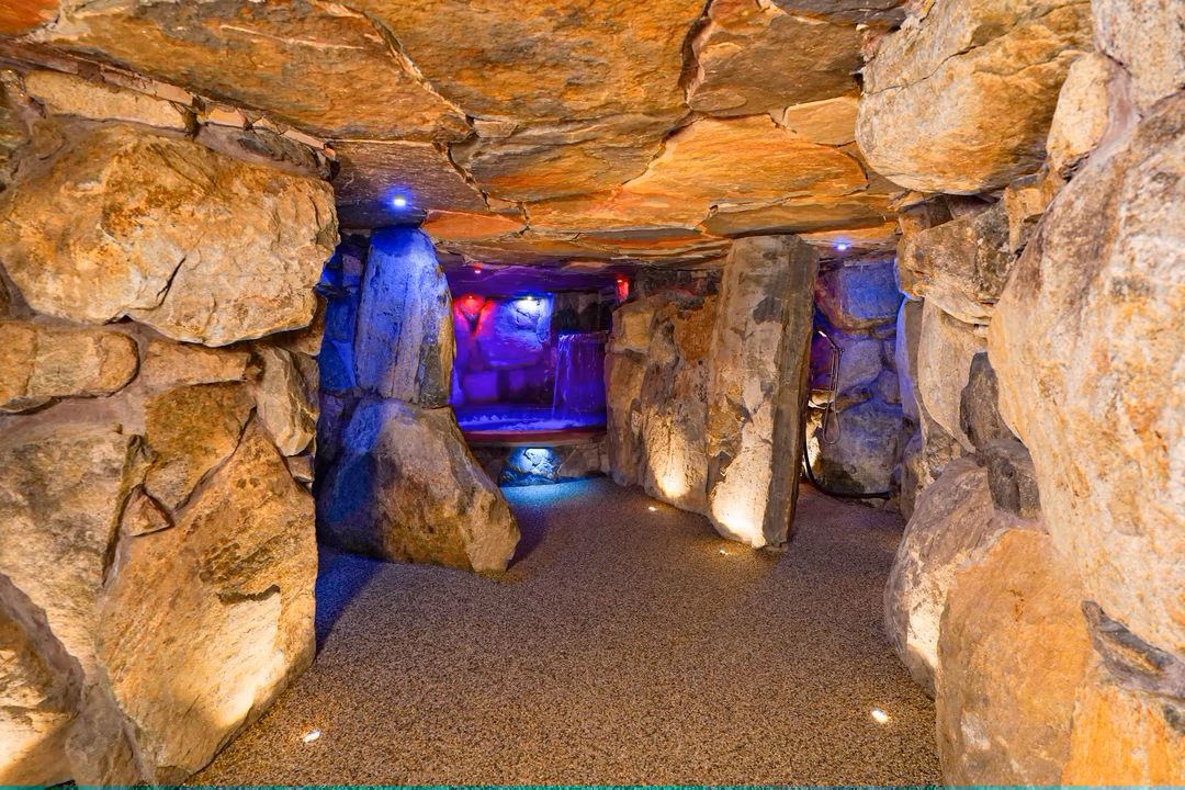 Sefinen Q - Finksburg, MD - This professionally constructed grotto features rough-hewn natural stone walls and ceiling creating an intimate, cave-like atmosphere. The centerpiece is a built-in pool with a cascading waterfall element that flows over large stone formations, enhanced by strategic blue LED lighting that accentuates the textures and creates a serene ambiance. The space demonstrates exceptional craftsmanship with seamless integration of the water feature into the stone structure, resulting in a luxurious and naturalistic outdoor living area.